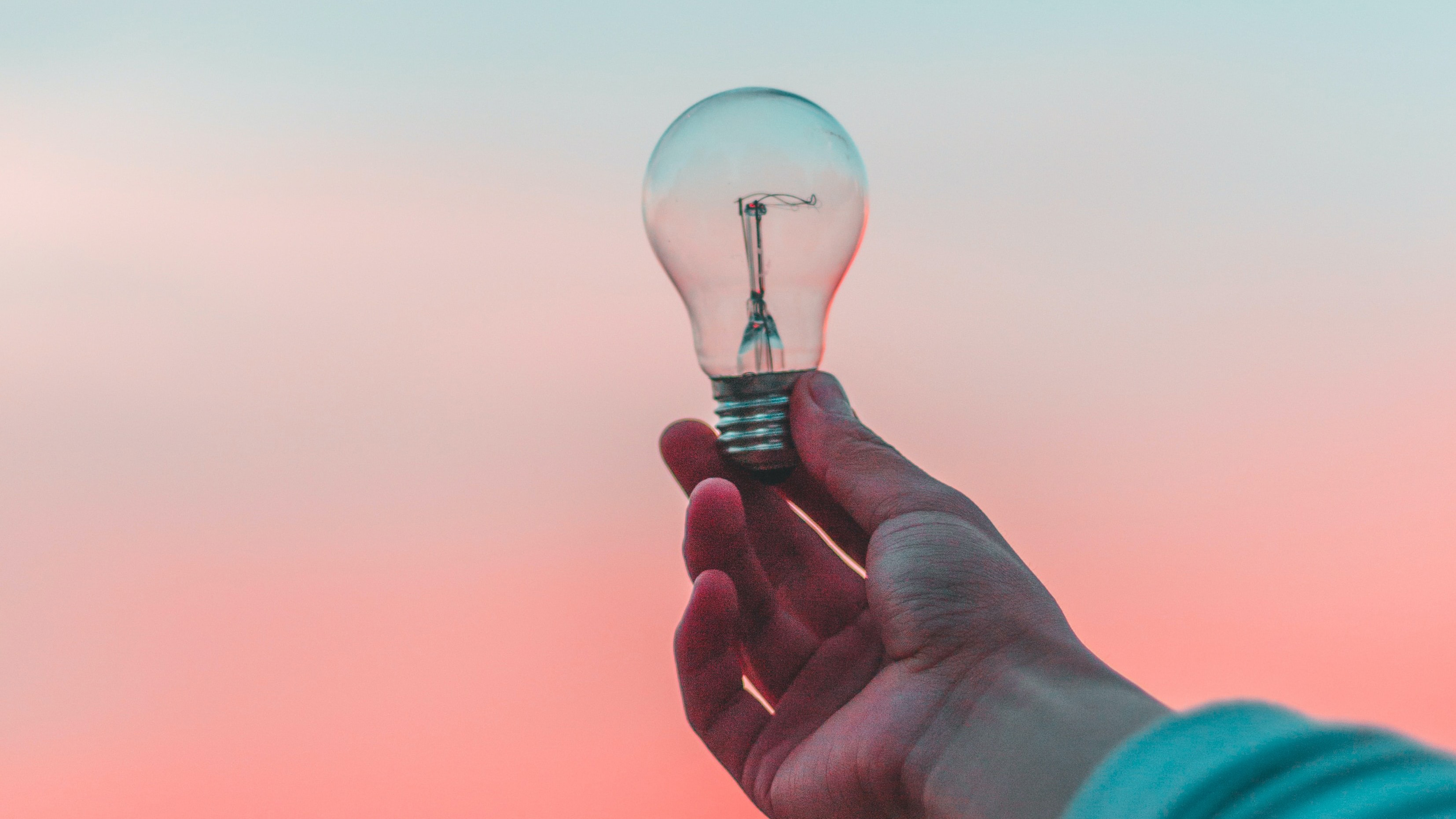 Person holding a lightbulb on a morning sunset.