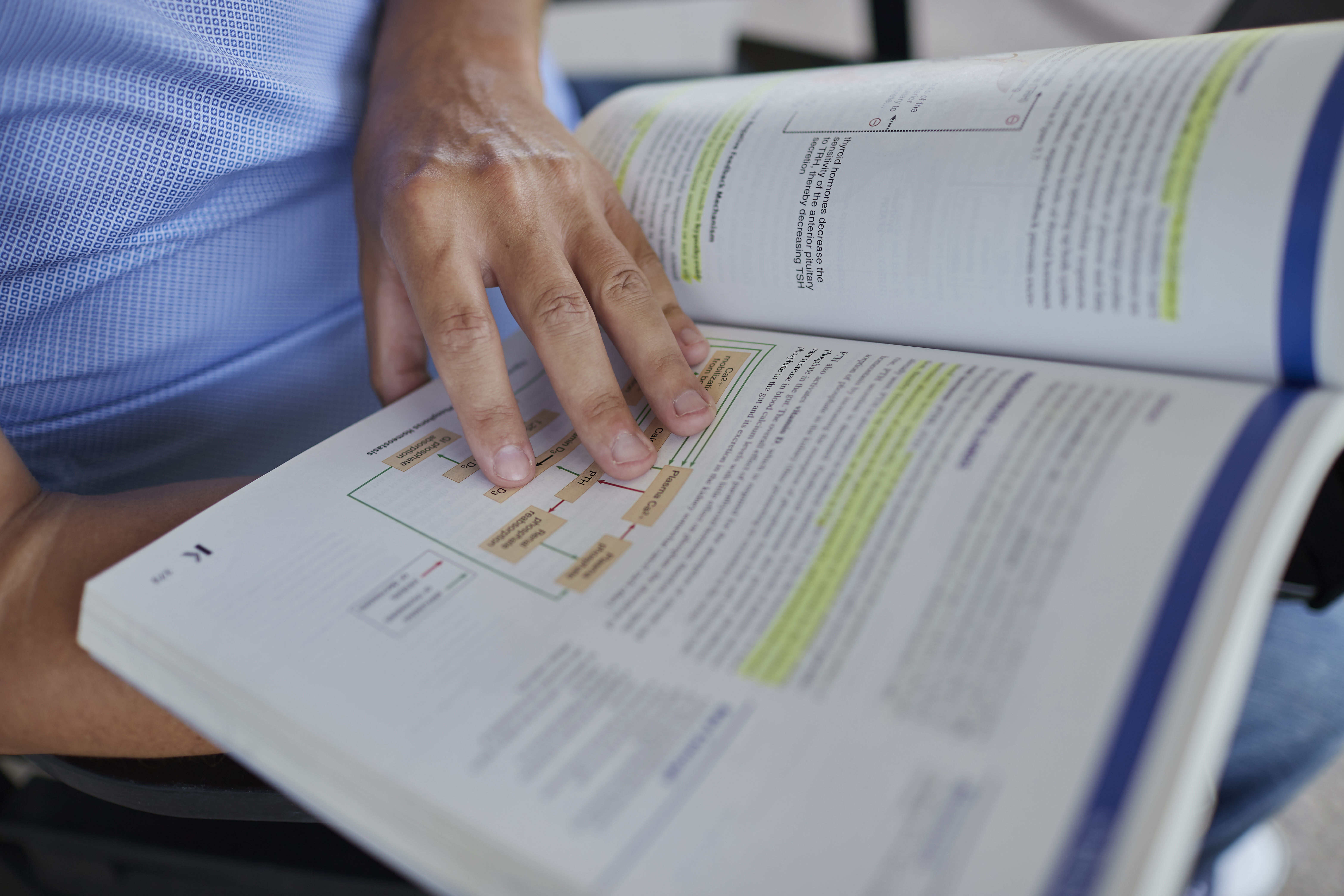 Close-up of a person reading an open book with highlighted text and diagrams.