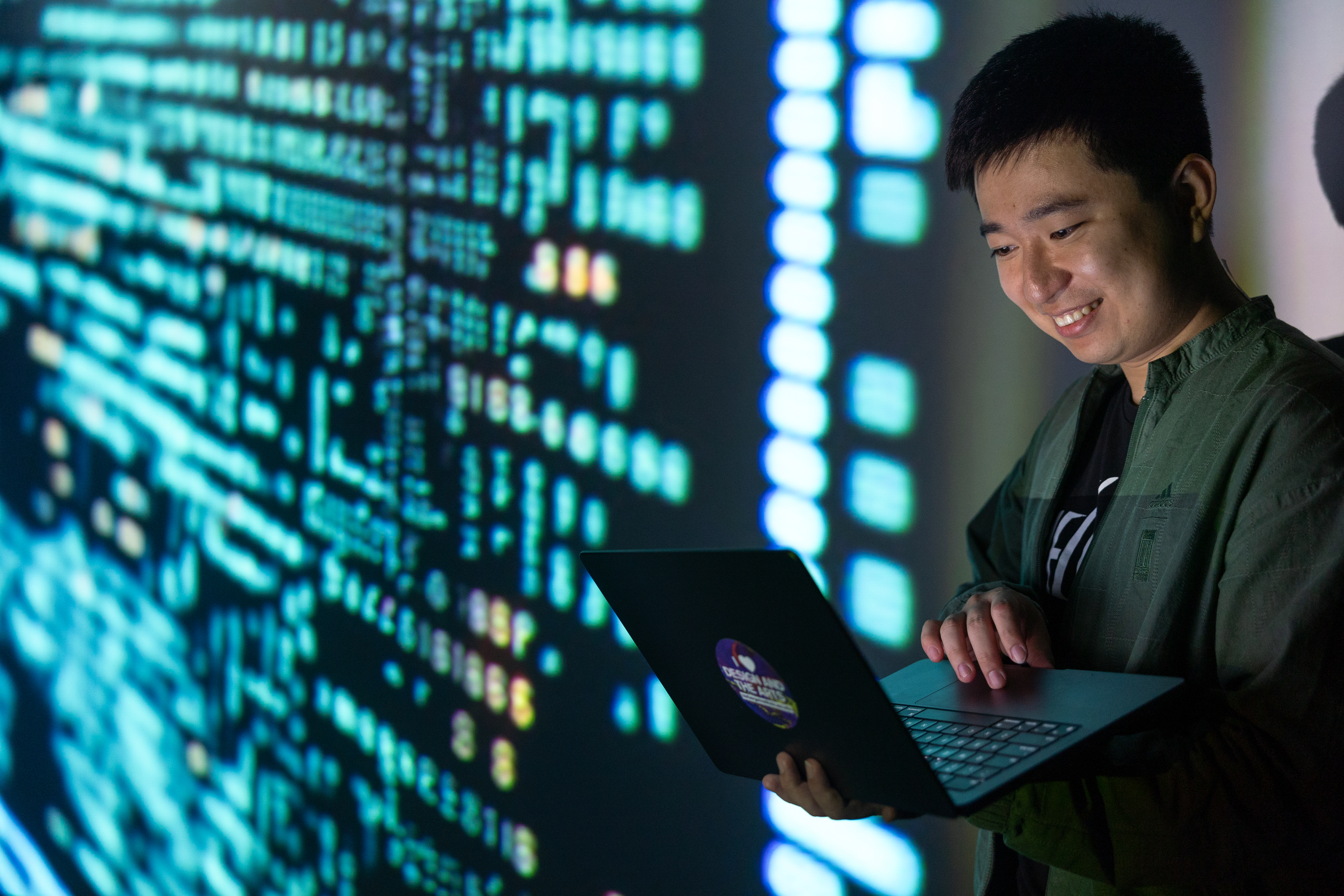 Person holding a laptop in front of a large display of illuminated code.