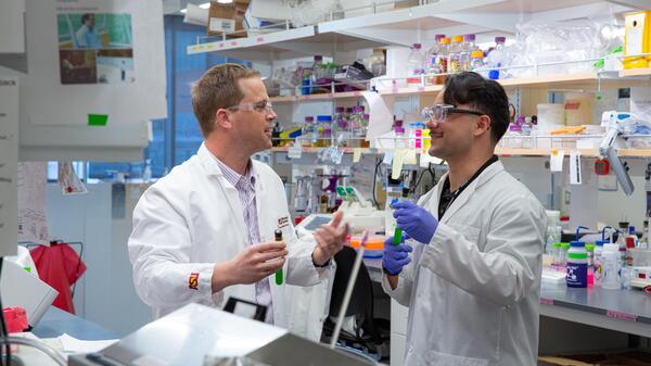 A student and professor engaging in dialogue in a biology lab. 