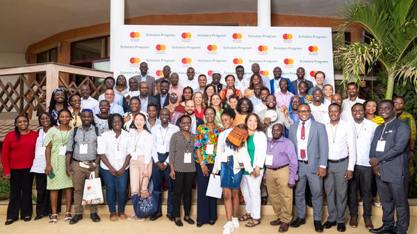 A large group of people poses together in front of a banner with "Scholars Program" logos.