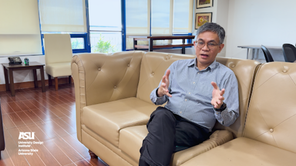 Bong Eliab sitting on a tan leather couch, wearing a blue shirt and black pants