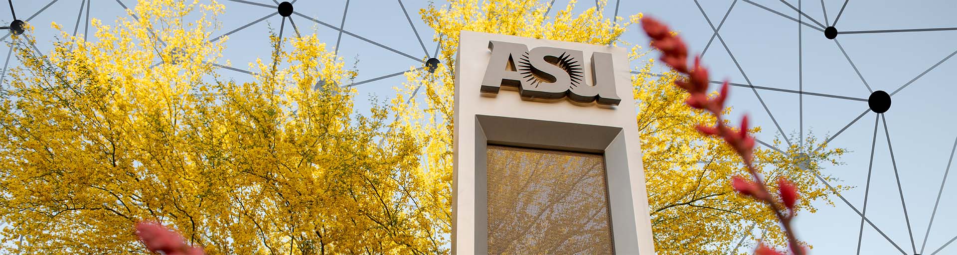 ASU sign with sunburst logo, yellow foliage, and geometric pattern above.