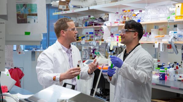 A student and professor engaging in dialogue in a biology lab.