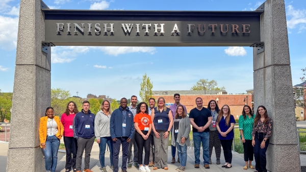 A group of higher education professionals from across the state of Connecticut gathered under a campus archway that reads ‘Finish With a Future.’